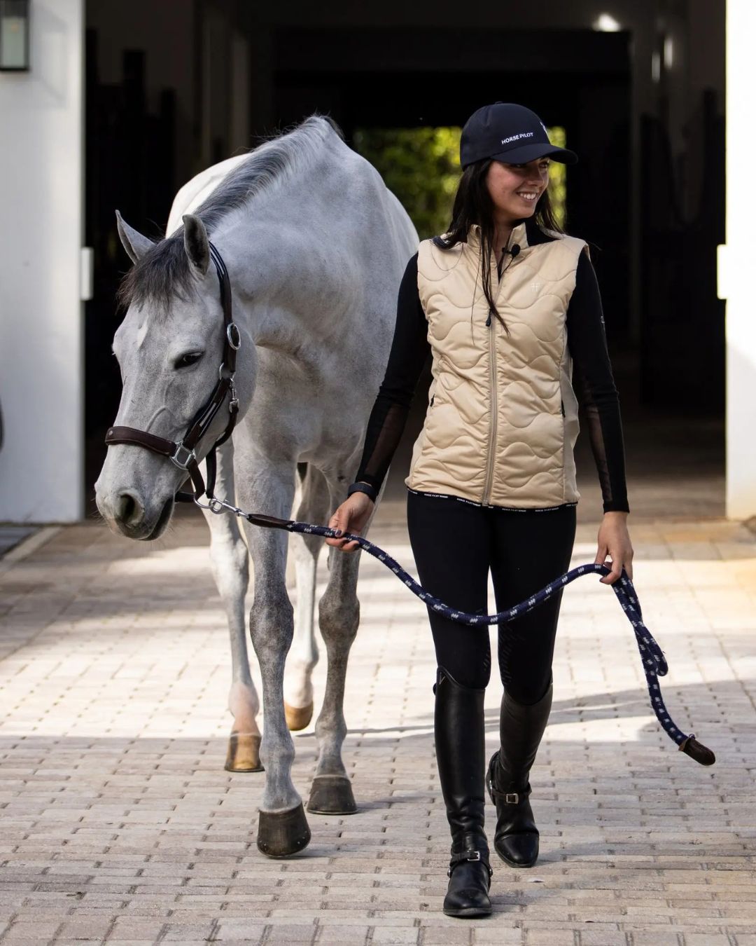 Horse Pilot Rider Vest - Latte, lifestyle image shown on woman walking gray horse | Equestrian Outerwear | Malvern Saddlery