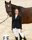 Pikeur Phelia Ladies Competition Dressage Coat - Black, shown on model standing next to horse in Dressage ring | Malvern Saddlery