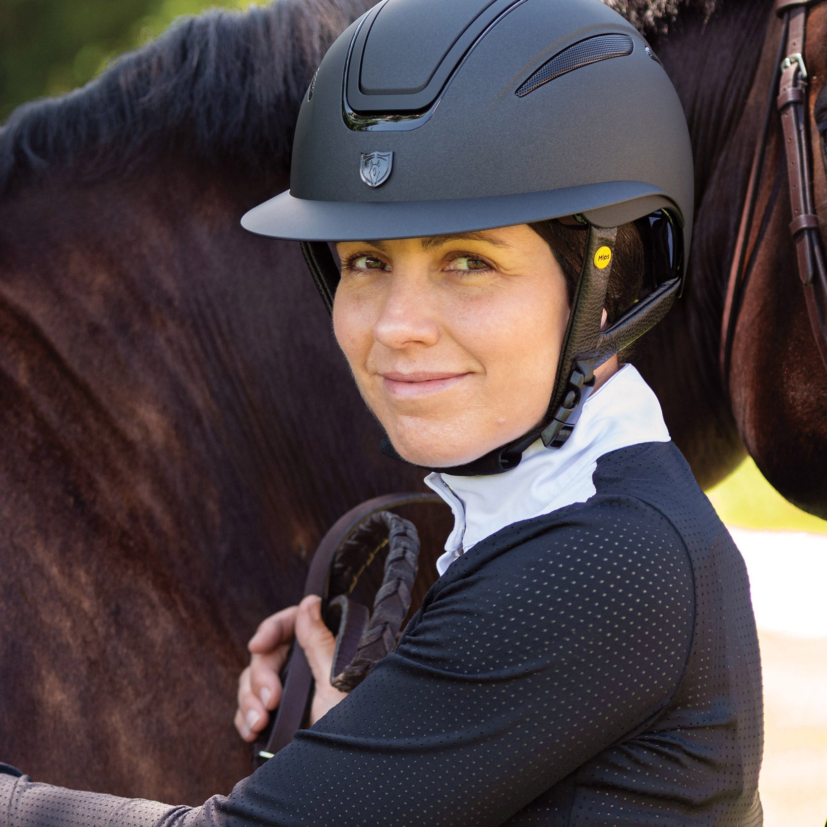 Tipperary Oxford Shimmer MIPS® Wide Brim Helmet - Black with Matte/Gloss trim; shown on rider next to horse | Equestrian Helmets | Malvern Saddlery
