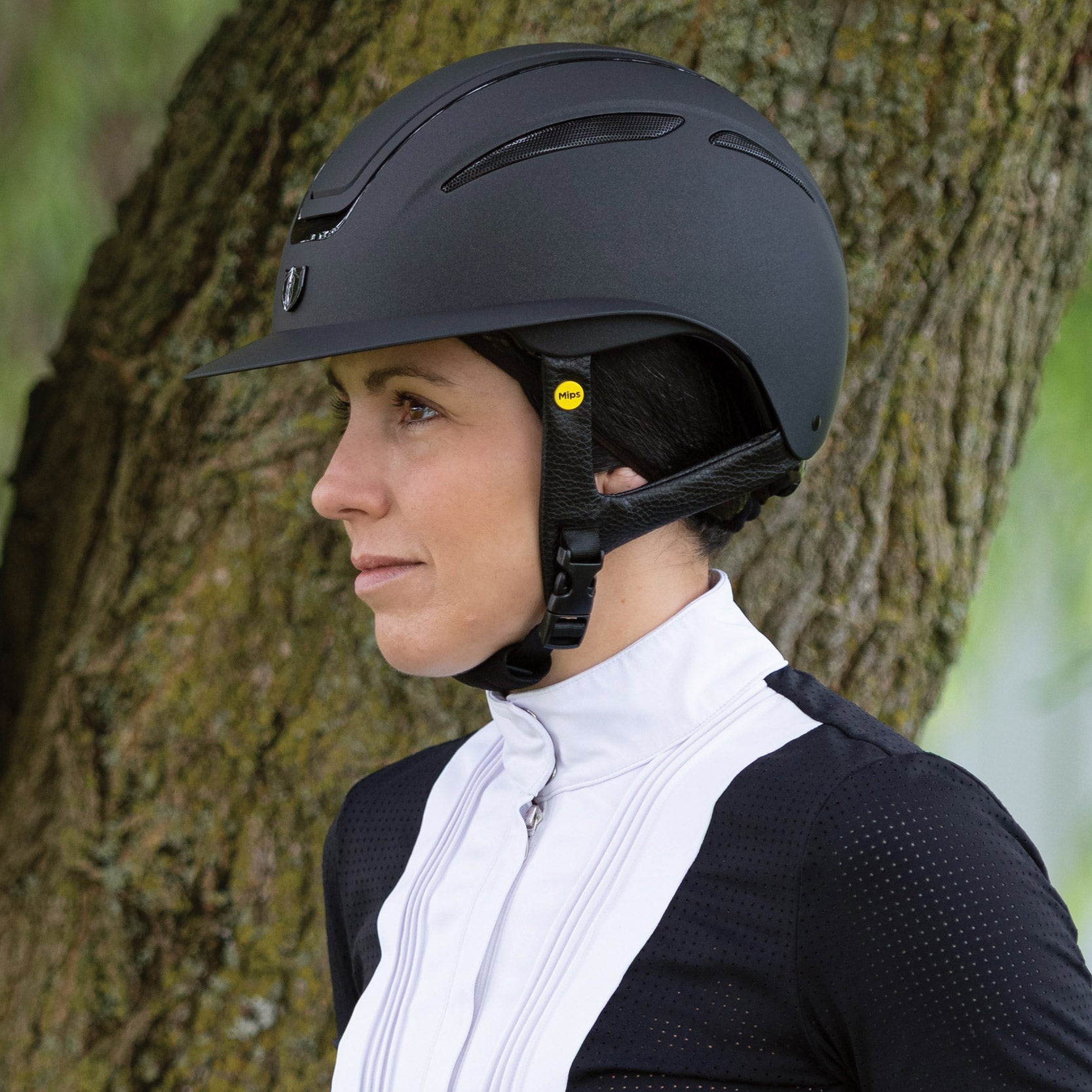 Tipperary Oxford Shimmer MIPS® Wide Brim Helmet - Black with Matte/Gloss trim; shown on rider outdoors next to tree | Equestrian Helmets | Malvern Saddlery