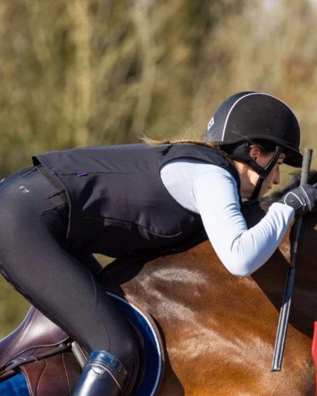 Person riding a horse in equestrian attire wearing Charles Owen Eclipse Back Protector with a blurred natural background | Malvern Saddlery