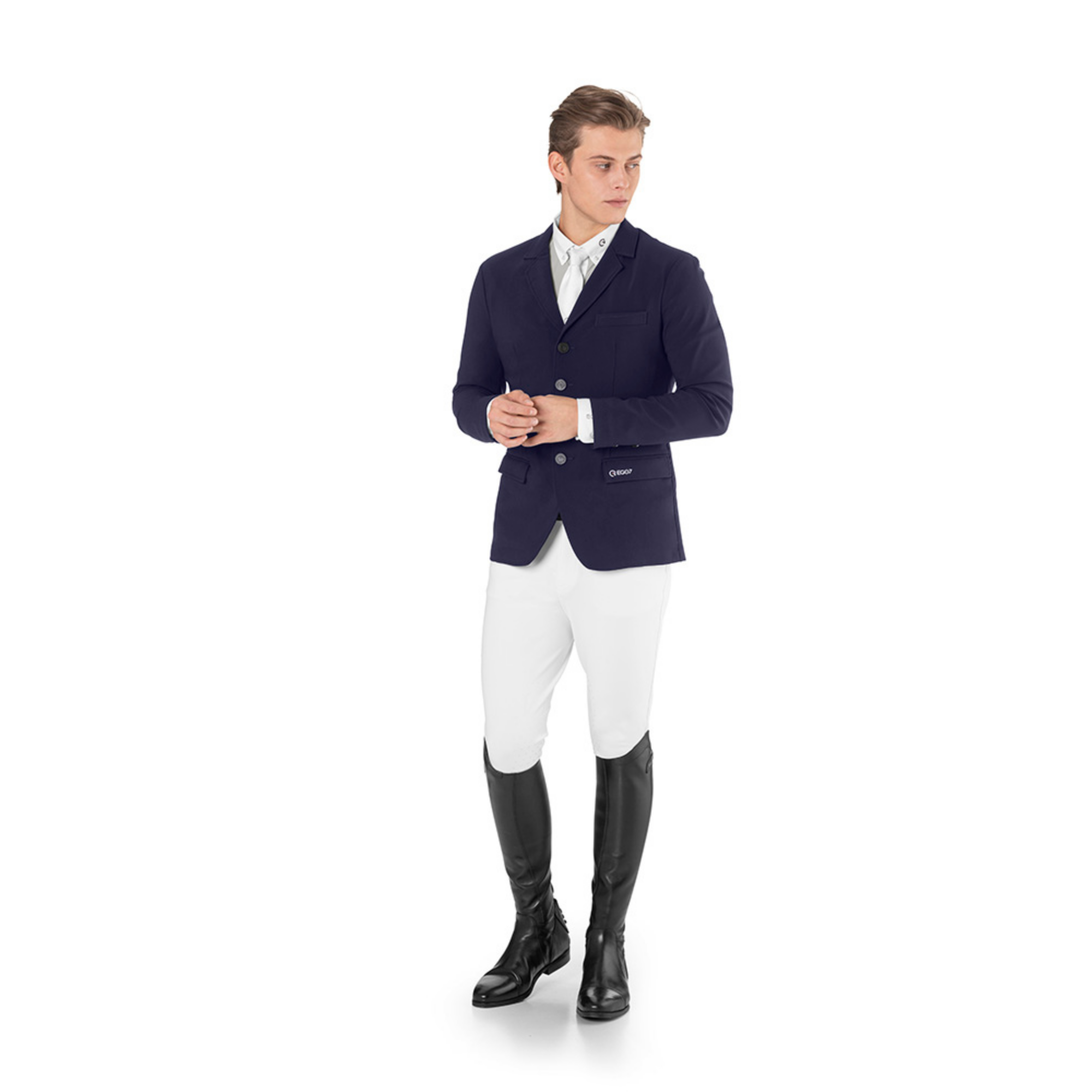 Male equestrian model standing against a white background wearing the EGO7 Be Air Men's Show Jacket in navy blue paired with white riding breeches and black tall boots.