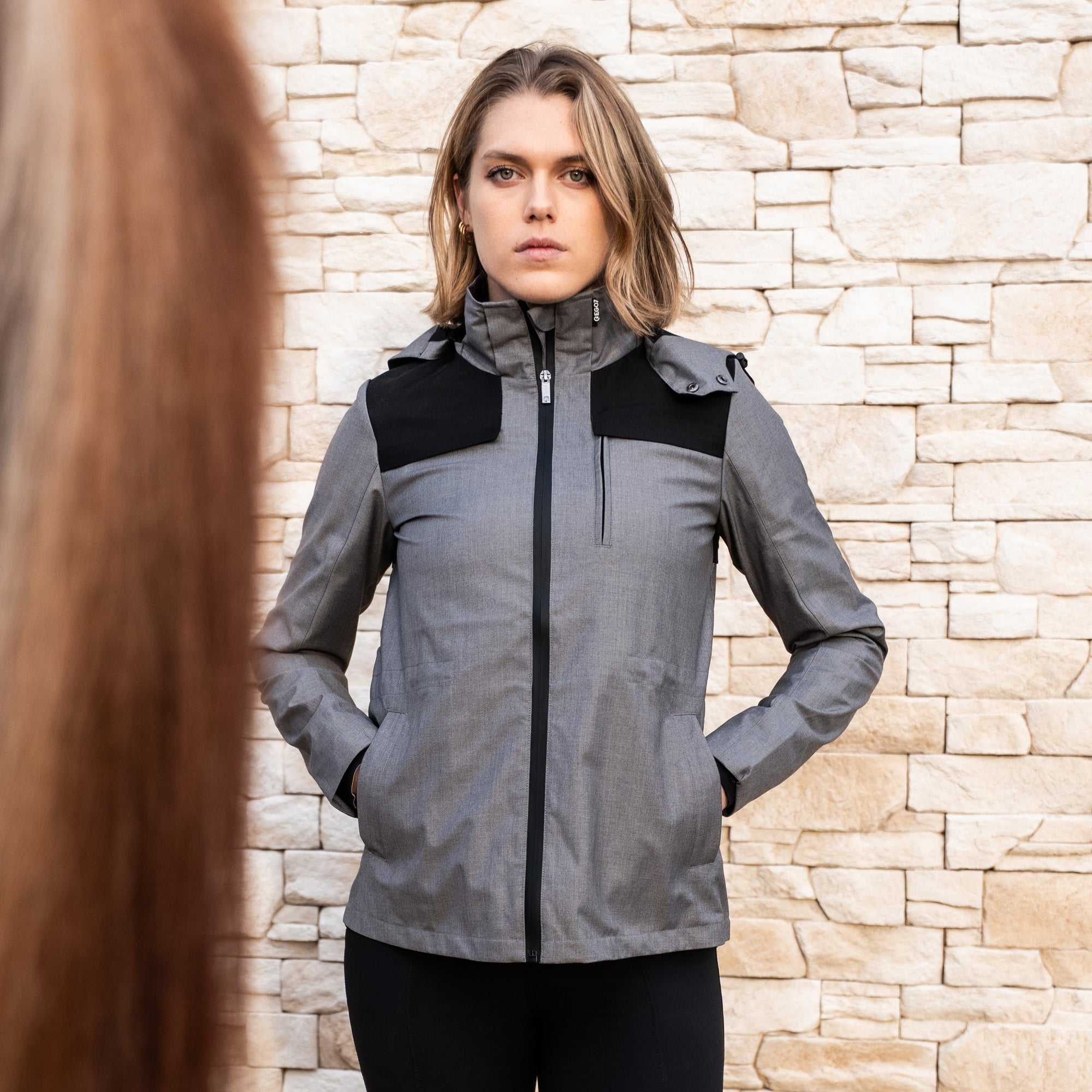 Female rider wearing the EGO7 Skye women's waterproof equestrian jacket in melange grey, standing next to a horse.