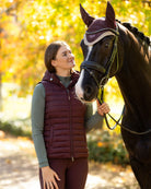 LeMieux Rose Hooded Puffer Vest - Damson Maroon, shown on woman standing next to horse with trees in background | Malvern Saddlery