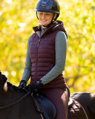LeMieux Rose Hooded Puffer Vest - Damson Maroon, shown on woman riding horse with trees in background | Malvern Saddlery
