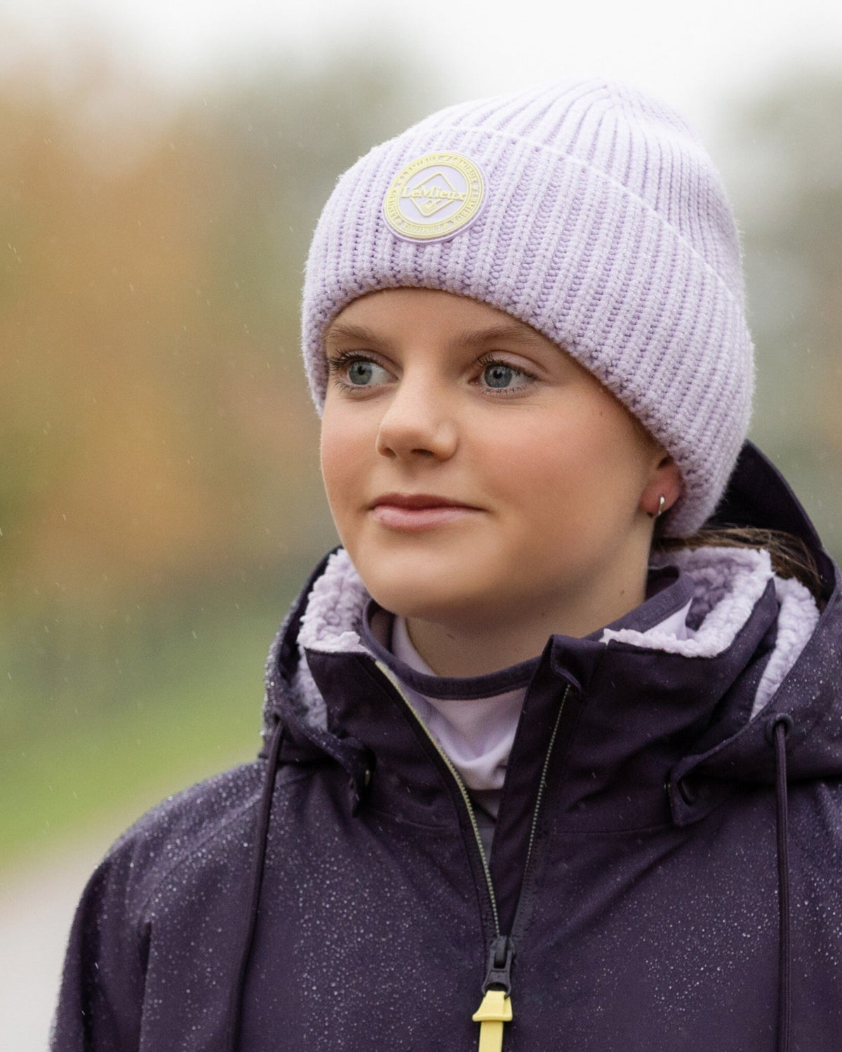 LeMieux Bodie Beanie - Lilac, shown on person wearing purple coat on trees in background | Winter Hats | Malvern Saddlery