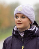 LeMieux Bodie Beanie - Lilac, shown on person wearing purple coat on trees in background | Winter Hats | Malvern Saddlery