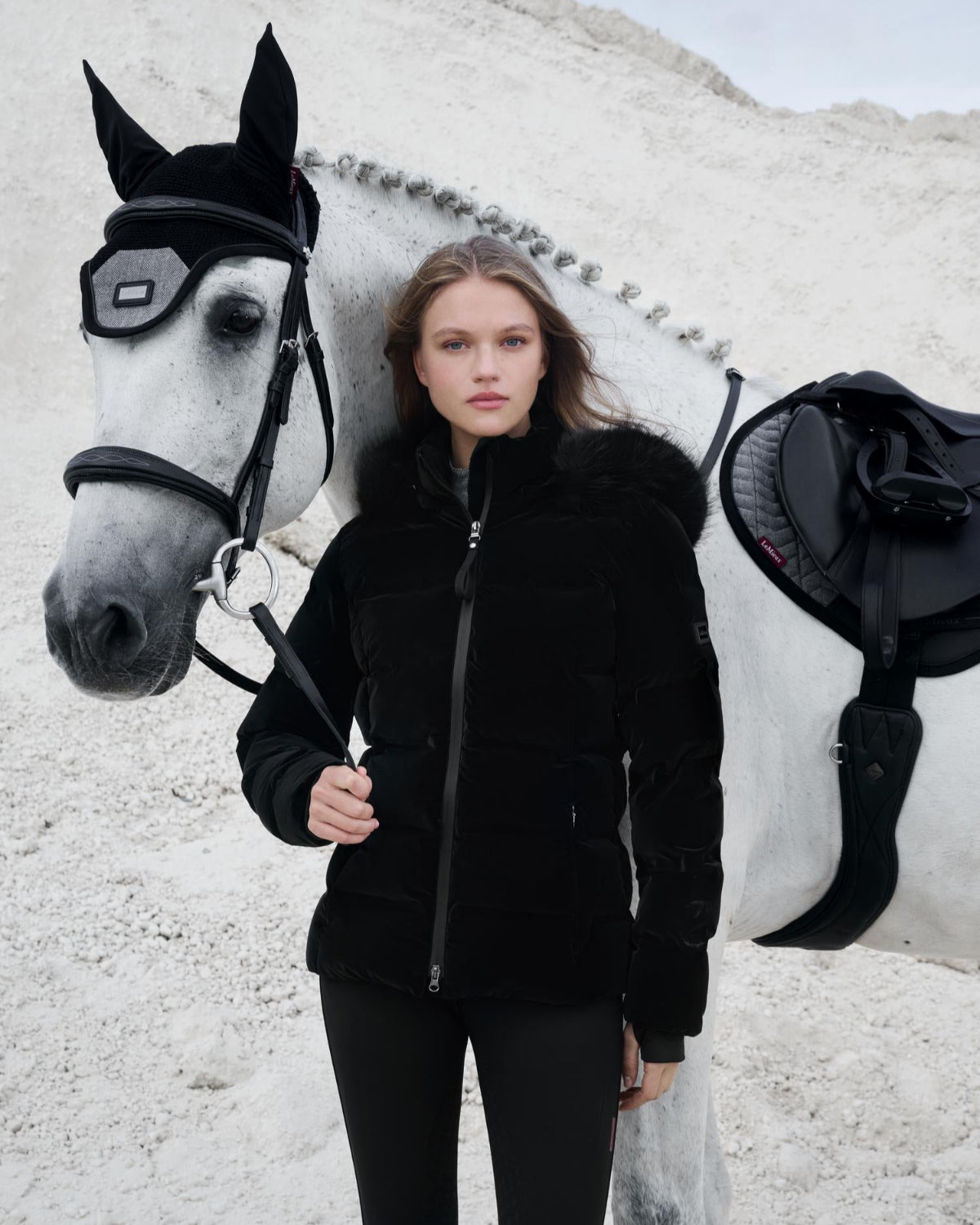 LeMieux Aspen Puffer Jacket - Black; shown on model standing next to horse with white surface background | Ladies' Outerwear | Malvern Saddlery