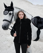 LeMieux Aspen Puffer Jacket - Black; shown on model standing next to horse with white surface background | Ladies' Outerwear | Malvern Saddlery