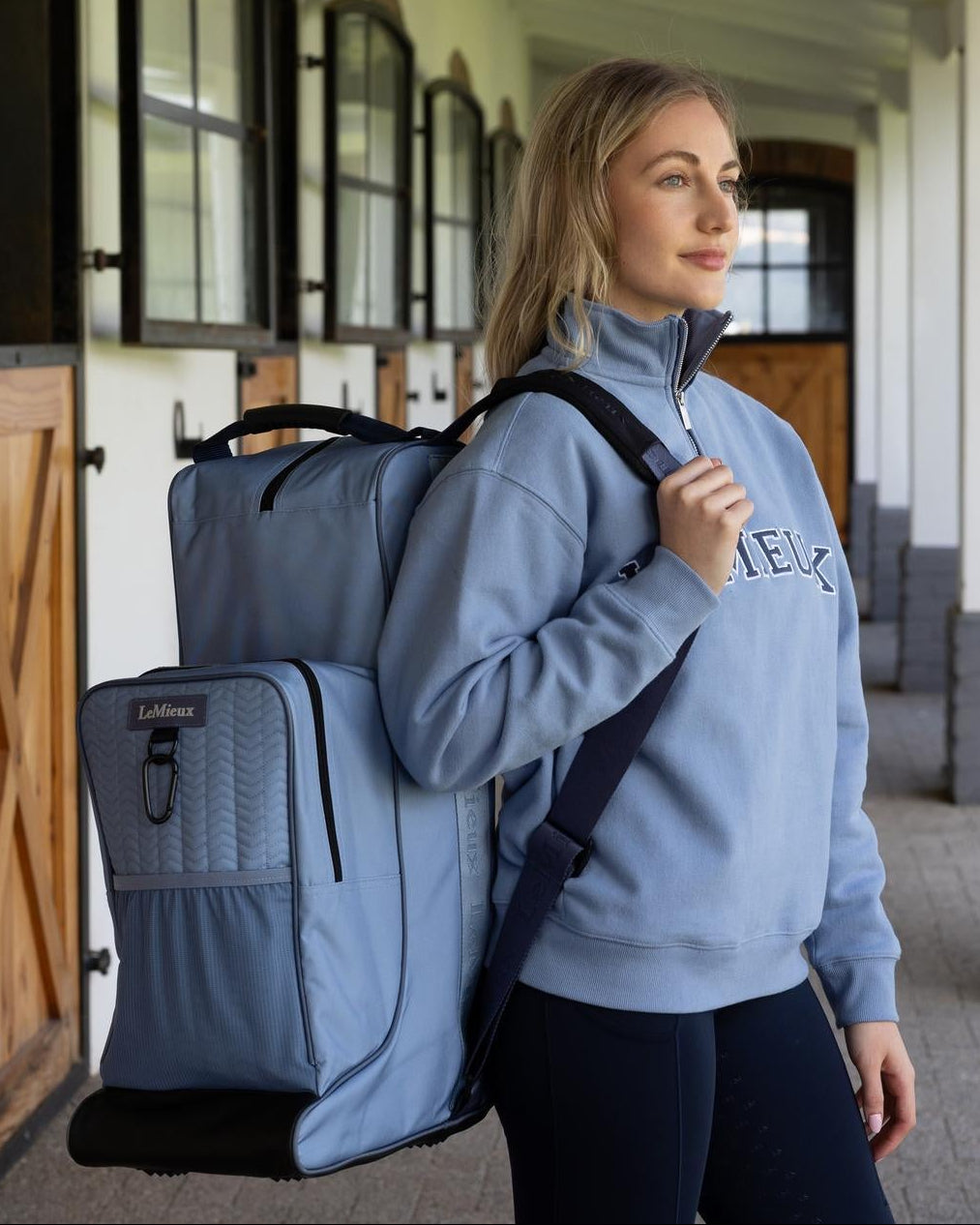 LeMieux Boot & Helmet Bag - Powder Blue; shown on person carrying on shoulder outside of stables | Malvern Saddlery
