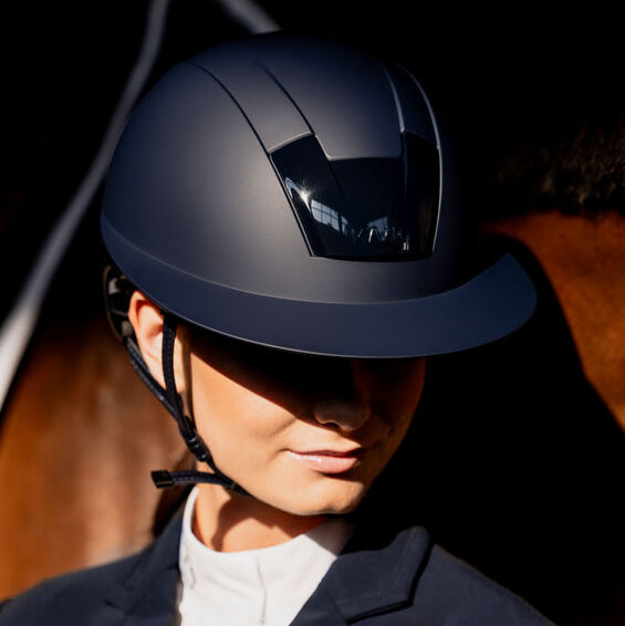 KASK Kooki Lady Helmet - Navy Matte, shown on rider wearing showcoat, horse in background | Malvern Saddlery
