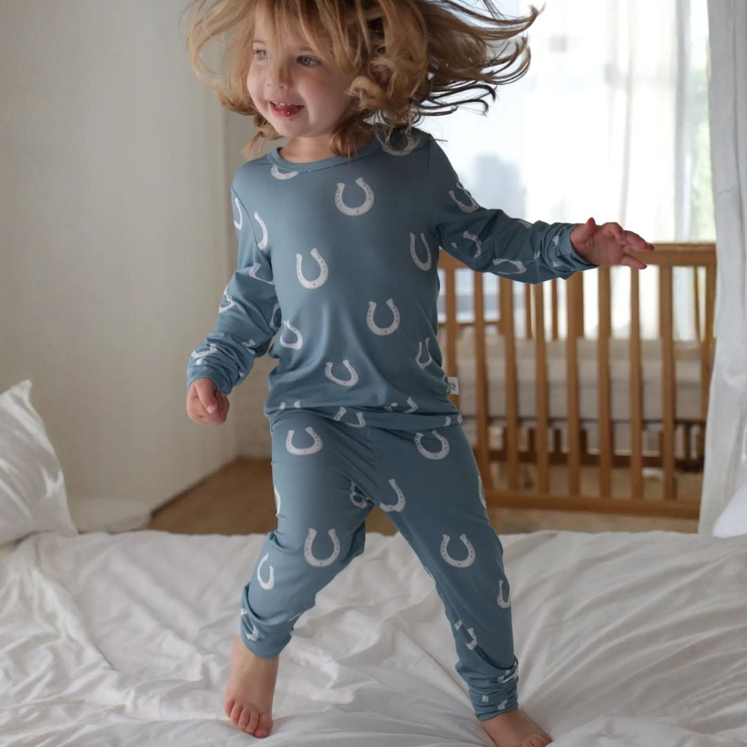 Kids Equestrian Horseshoe Pajamas - Blue; shown on kid jumping on bed | Malvern Saddlery