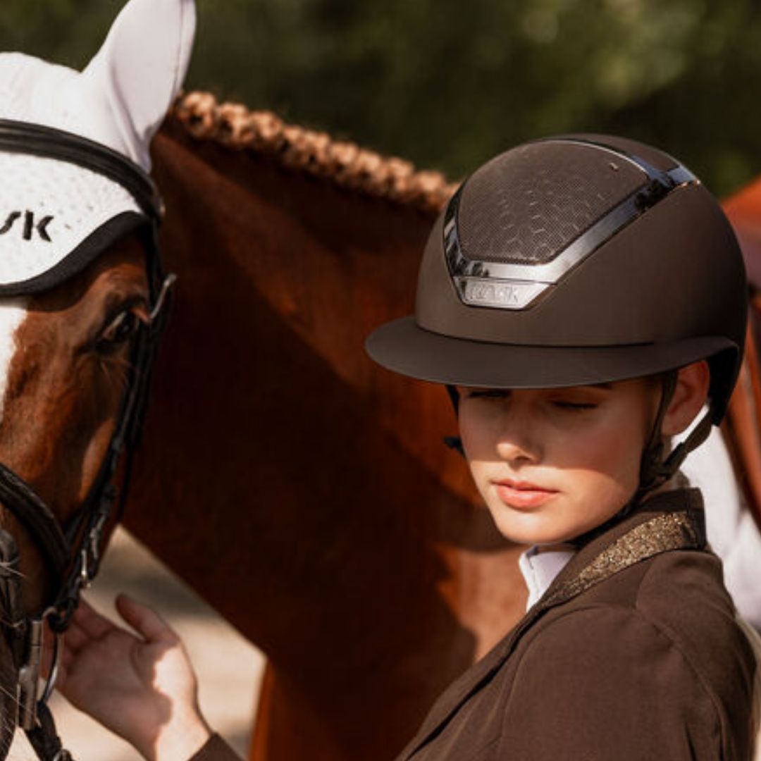 KASK Star Lady Chrome Equestrian Helmet - Brown; close up shown on woman wearing showcoat next to chestnut horse | Wide Brim English Riding Helmets | Malvern Saddlery