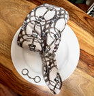 Equestrian Snaffle Bit Status Print Cloth Napkin, shown on white plate with bit accent & pewter fox napkin ring | Malvern Saddlery