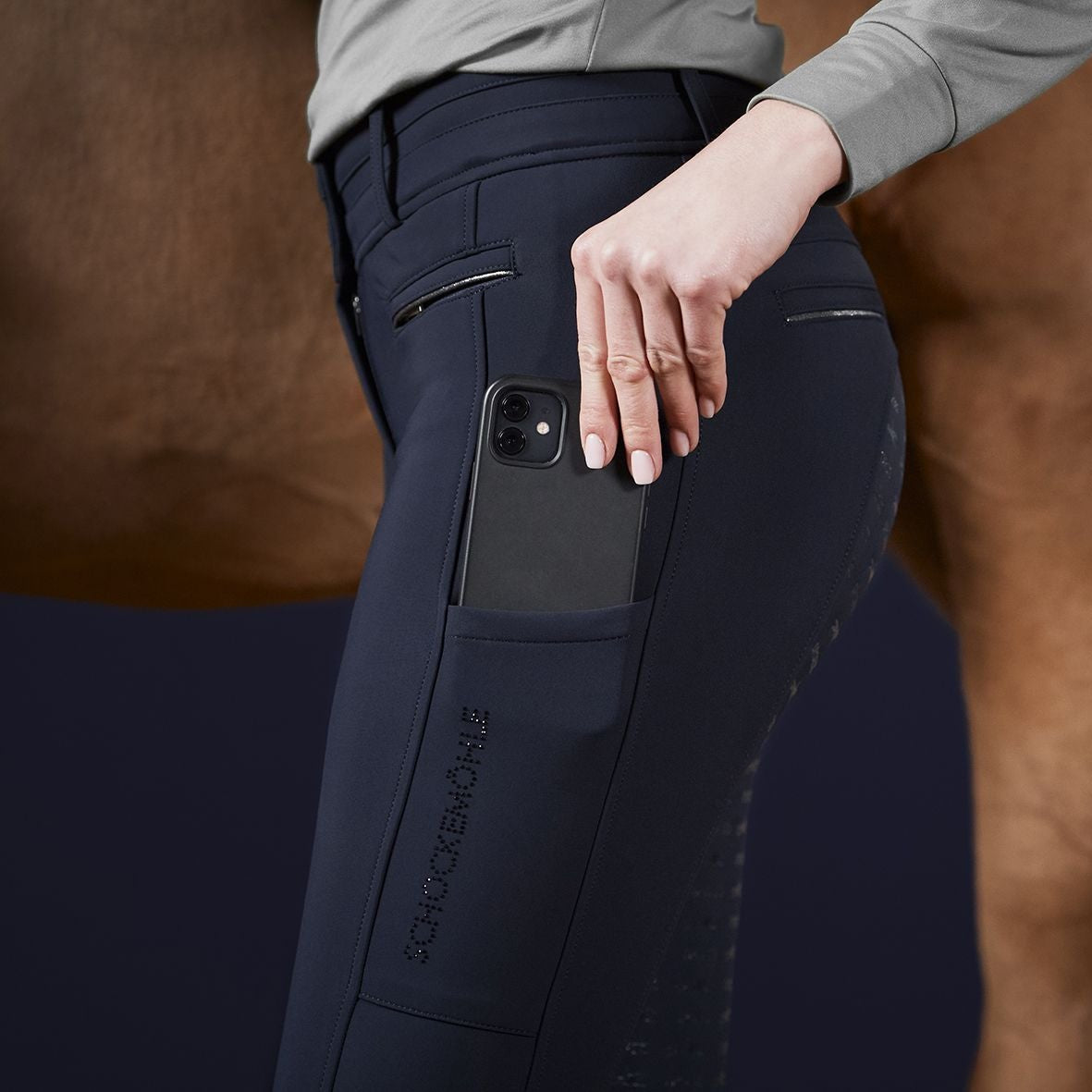 Schockemoehle Ladies Winter Heather Breech - Navy; on woman detail placing phone in leg pocket | Full Seat Breeches | Malvern Saddlery