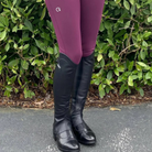EGO7 Lyra black leather equestrian half chaps worn over paddock boots with plum riding breeches outdoors, three-quarter front angle view