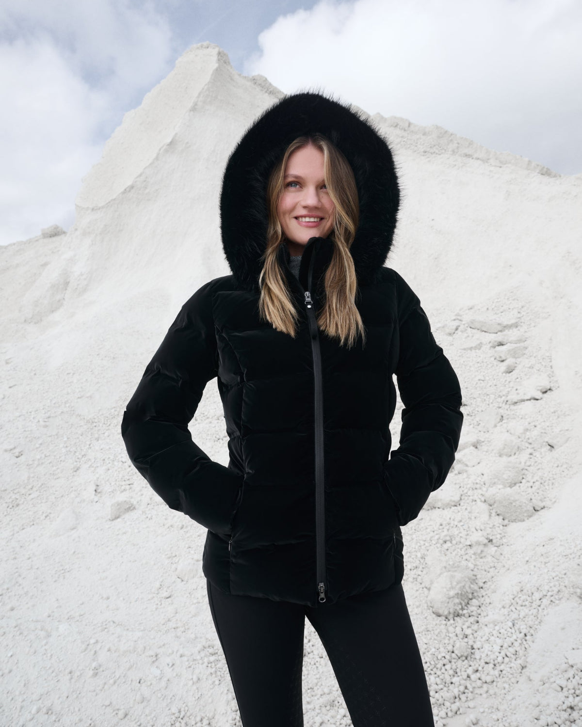 LeMieux Aspen Puffer Jacket - Black; shown with hood up on model with clouds and white surface background  | Ladies' Outerwear | Malvern Saddlery