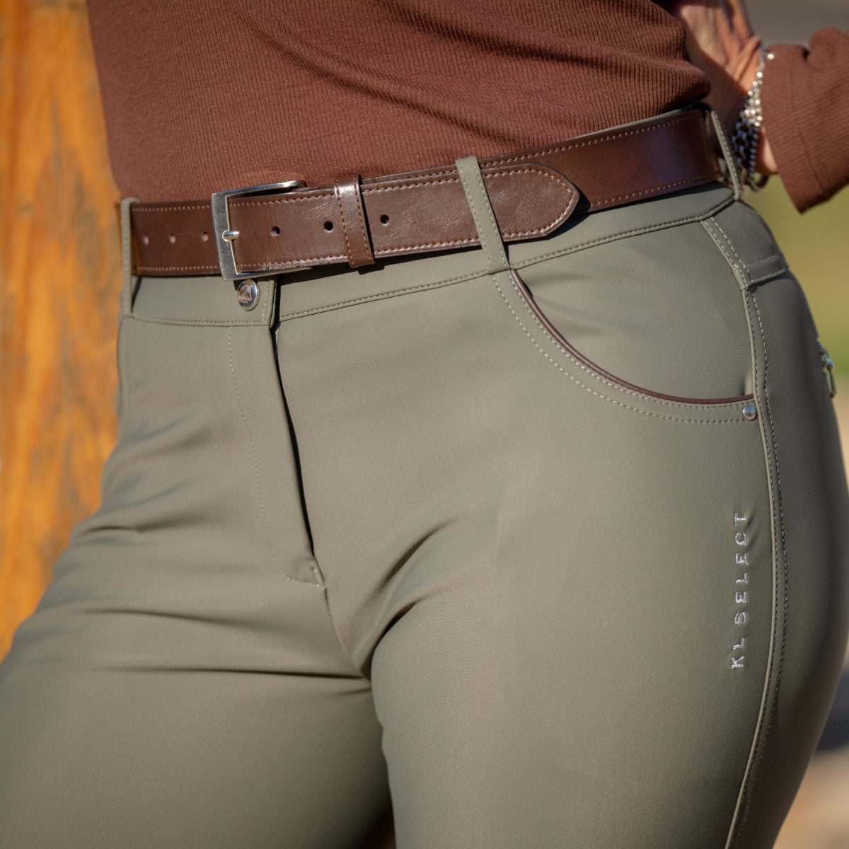 KL Select Gabrielle Knee Grip Breeches - Olive with Espresso details; close up on model blurred outdoor background | Women's Riding Apparel  | Malvern Saddlery