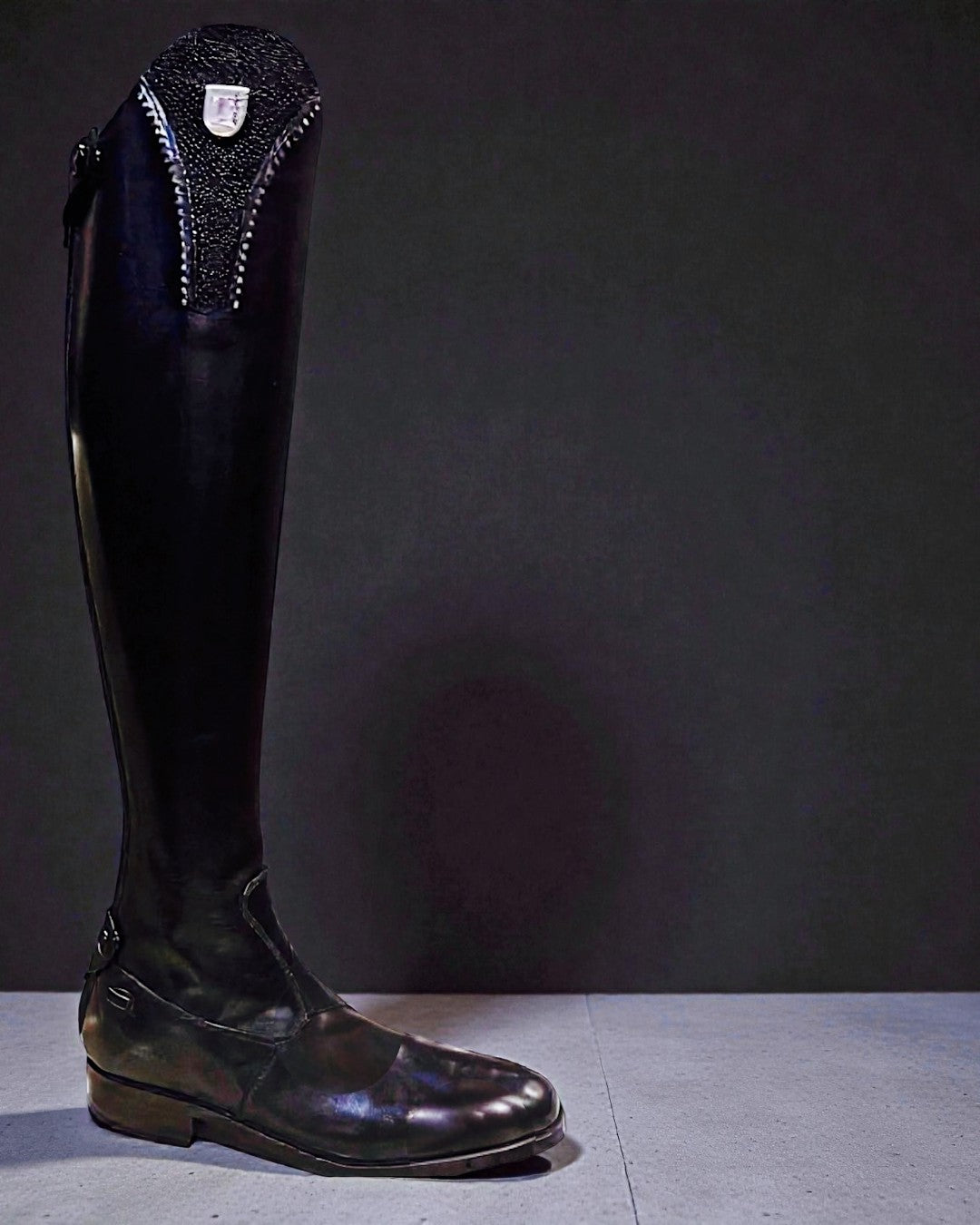 Black Tucci riding boot with decorative top on a dark background