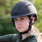 Tipperary Oxford Shimmer MIPS® Wide Brim Helmet - Black with Glimmer/Gloss trim; shown on rider with blurred outdoor background | Equestrian Helmets | Malvern Saddlery