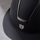 Tipperary Equestrian Windsor MIPS® Wide Brim Helmet; Black Matte with Smoked Chrome; close up of front logo and visor | Malvern Saddlery