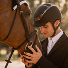 Kask Dogma Chrome Equestrian Helmet - Brown; shown on rider with horse blurred outside background | Malvern Saddlery