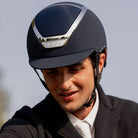 Kask Dogma Chrome Equestrian Helmet - Navy Matte with Silver Frame;  close up shown on man with sky background | Standard Brim English Riding Helmets | Malvern Saddlery