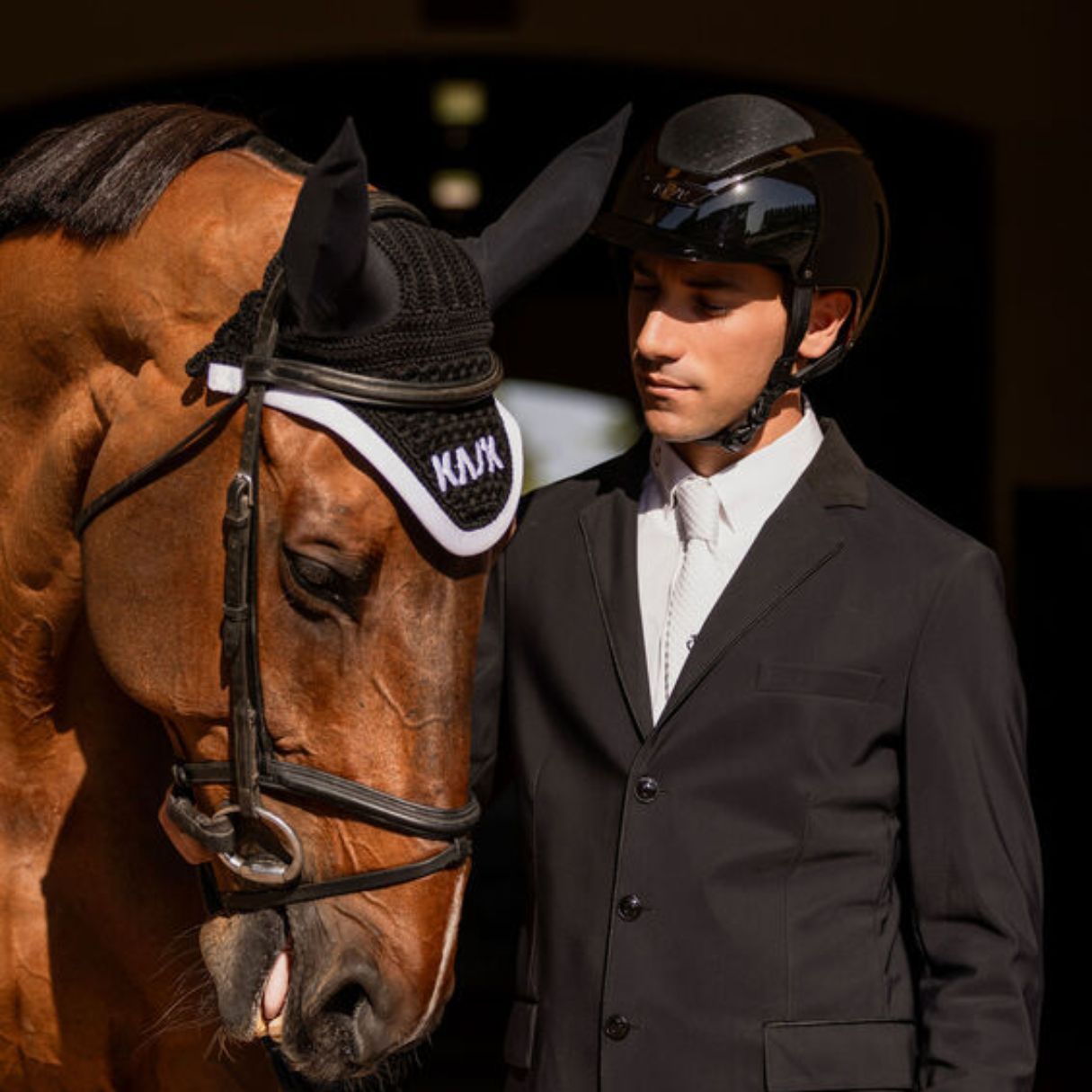 Kask Equestrian Dogma Pure Shine Helmet - Black; shown on rider wearing showcoat standing with horse| Standard Brim Helmets | Malvern Saddlery