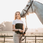 Female rider standing next to a grey horse wearing the black EGO7 Mesh Women's Short Sleeve Show Shirt with white shoulders and stand-up collar