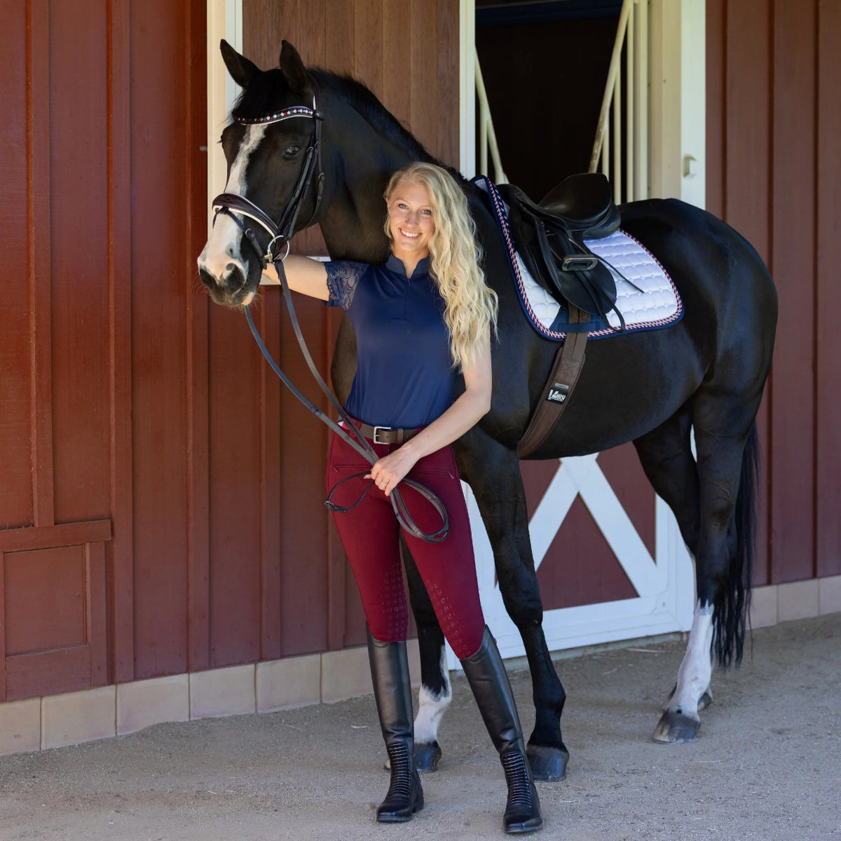 Halter Ego Kimberly Knee Grip Breeches - Burgundy; worn by woman standing next to horse by barn | Malvern Saddlery