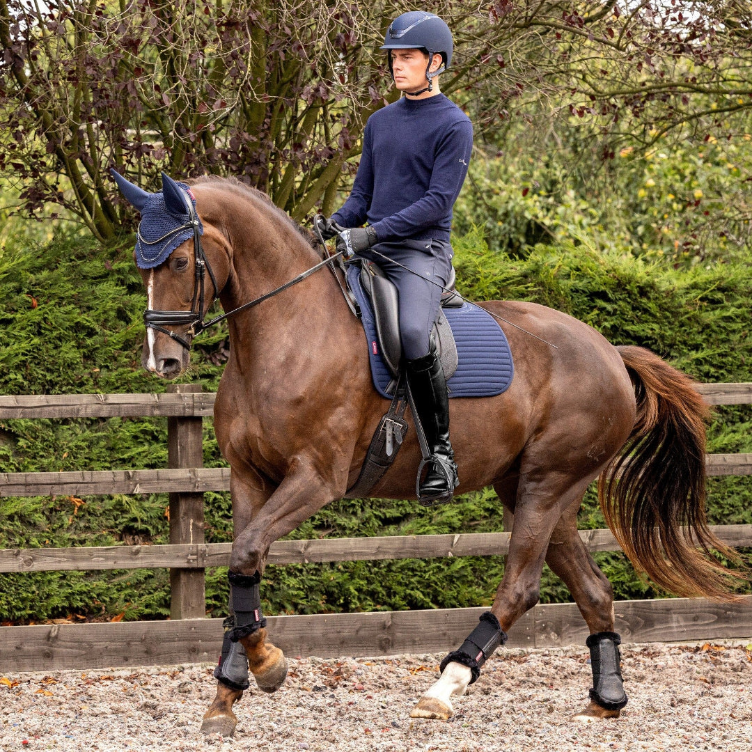 LeMieux Soft Shell Anti Slip Dressage Saddle Pad - Navy; Person riding a horse in an outdoor equestrian setting with a wooden fence and greenery | Tack Shop | Malvern Saddlery