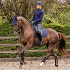 LeMieux Soft Shell Anti Slip Dressage Saddle Pad - Navy; Person riding a horse in an outdoor equestrian setting with a wooden fence and greenery | Tack Shop | Malvern Saddlery
