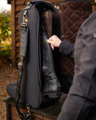 LeMieux Luxe Boot Bag - Black - person putting boot into brown faux fur lined compartment, outdoors | Rider Travel Bags | Malvern Saddlery