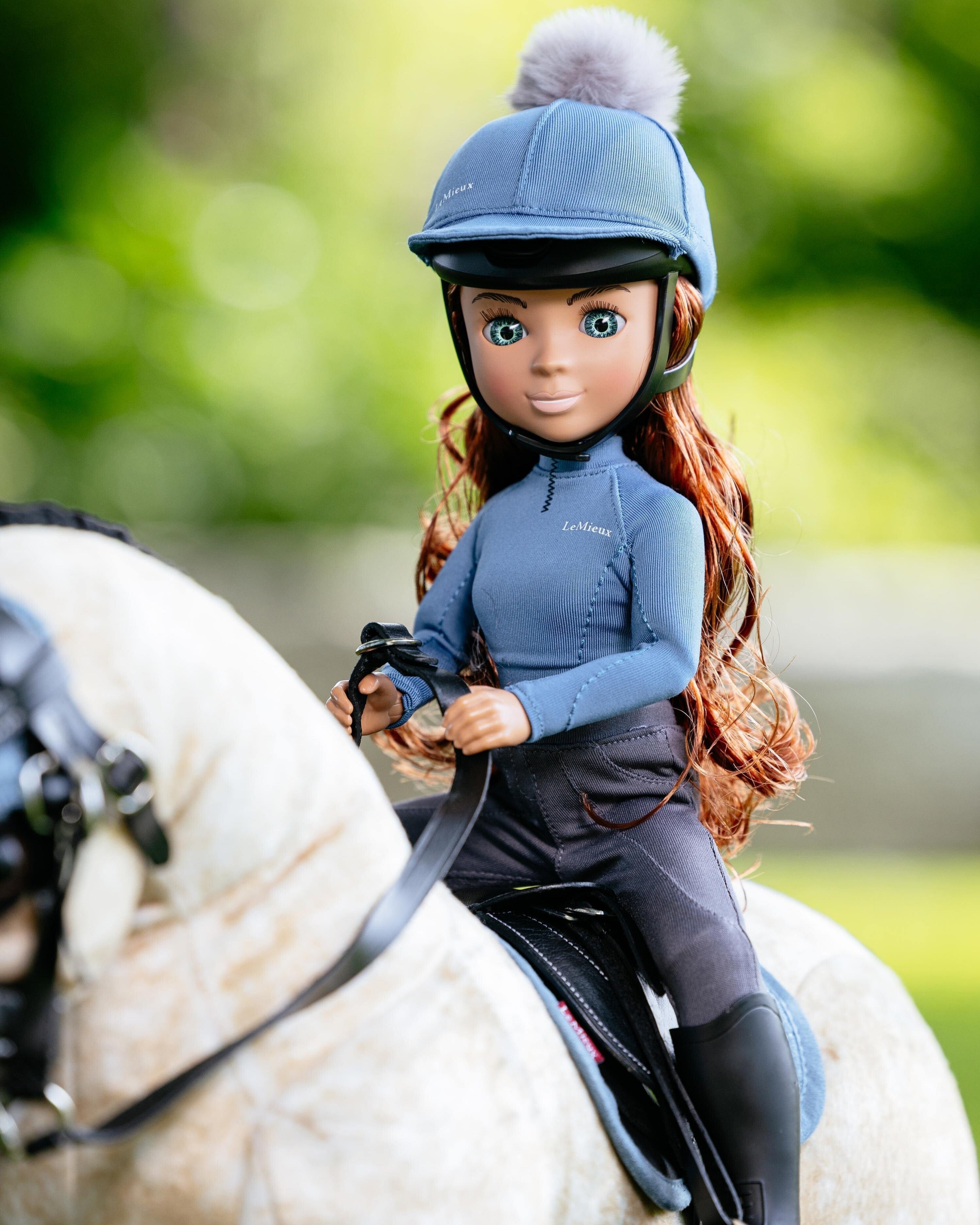 LeMieux Toy Pony Rider Doll - Olivia  in equestrian attire sitting on a horse with a blurred green background | Malvern Saddlery