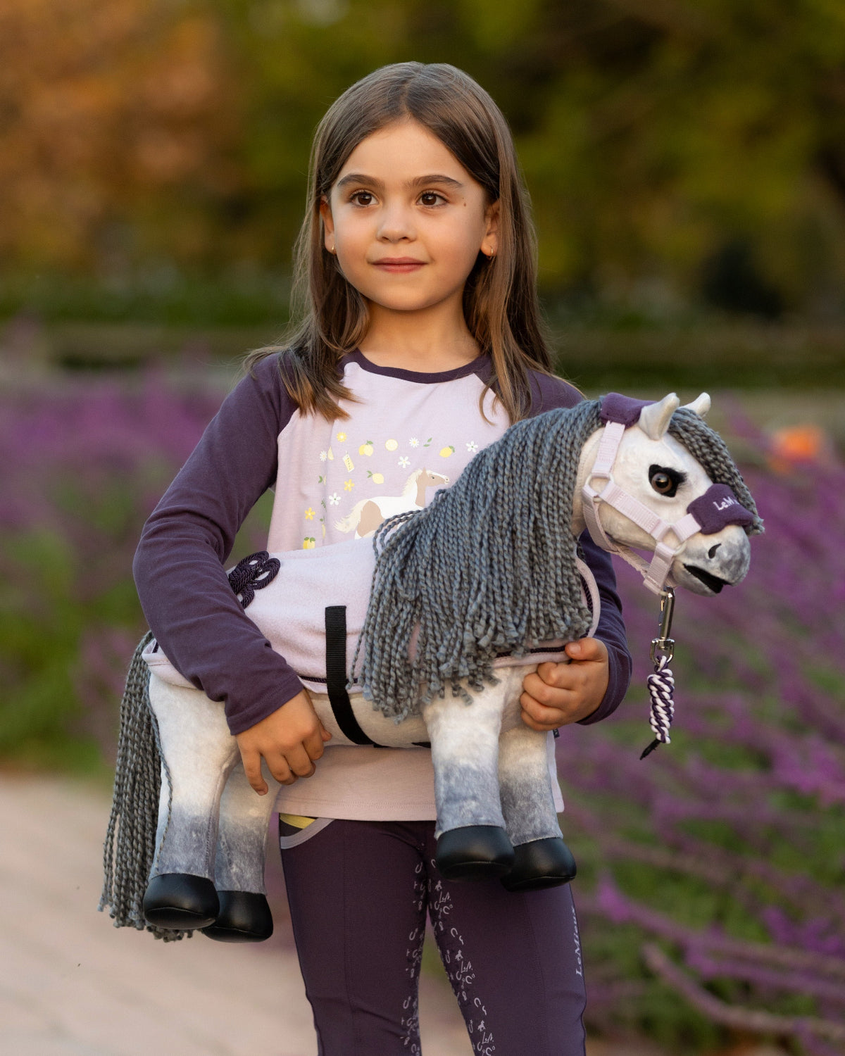 LeMieux Toy Pony Blanca - Young girl holding a toy horse with a blurred background of lavender fields | Malvern Saddlery