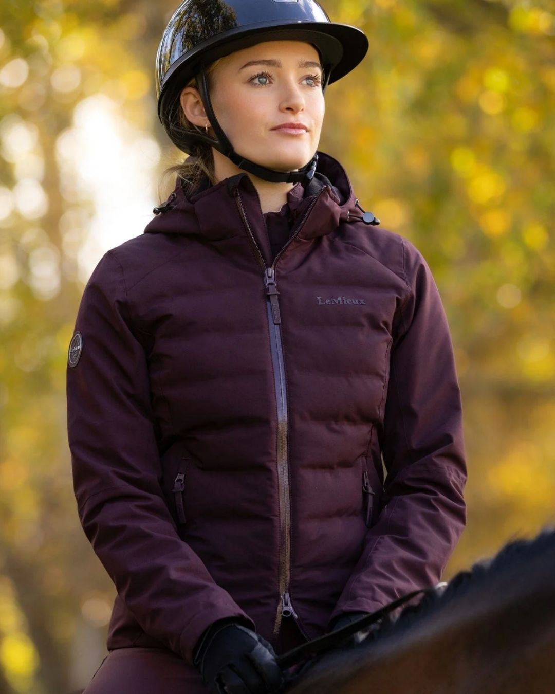 LeMieux Brooke Waterproof Hybrid Jacket - Damson [maroon] - shown on woman outdoors sitting on horse | Ladies' Outerwear | Malvern Saddlery