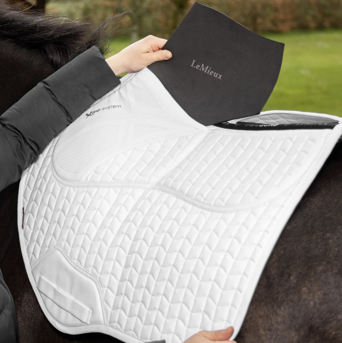 LeMieux ProSorb Plain 2 Pocket Close Contact Square Saddle Pad - White, on horse with person inserting pad into front pocket, outdoor background | Tack Shop | Malvern Saddlery