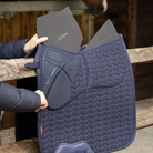 LeMieux ProSorb Plain 2 Pocket Dressage Square Saddle Pad - Navy, shown with pads being inserted on wooden fence, stable in background | Tack Shop | Malvern Saddlery
