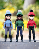 LeMieux Toy Pony Rider Dolls - Three dolls in equestrian outfits with colorful hats standing on a road with a blurred natural background | Malvern Saddlery