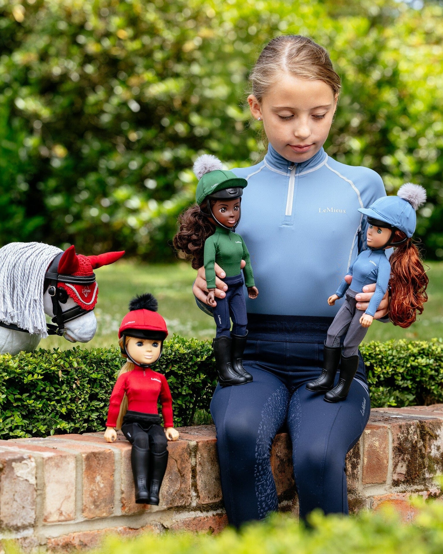 LeMieux Toy Pony Rider Dolls - Girl sitting on a stone wall with horse and multiple dolls in equestrian outfits | Malvern Saddlery