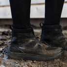 Close-up of black LeMieux Cavara Performance High Top Trainers being worn in muddy conditions around the stables.