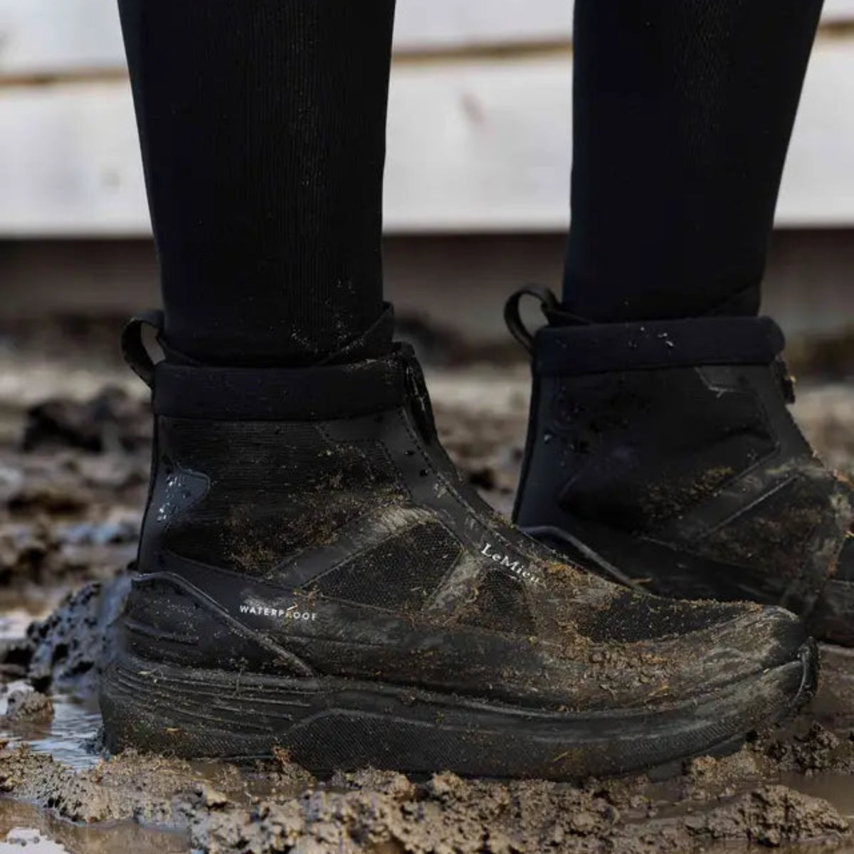 Close-up of black LeMieux Cavara Performance High Top Trainers being worn in muddy conditions around the stables.