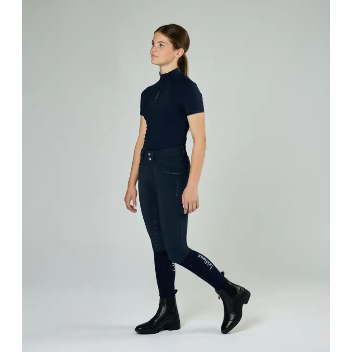 Young rider wearing black LeMieux Junior Zip Paddock Boots with dark navy breeches and top