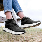 Lifestyle view of person wearing black LeMieux Kanta Waterproof Sneakers with denim jeans outdoors.