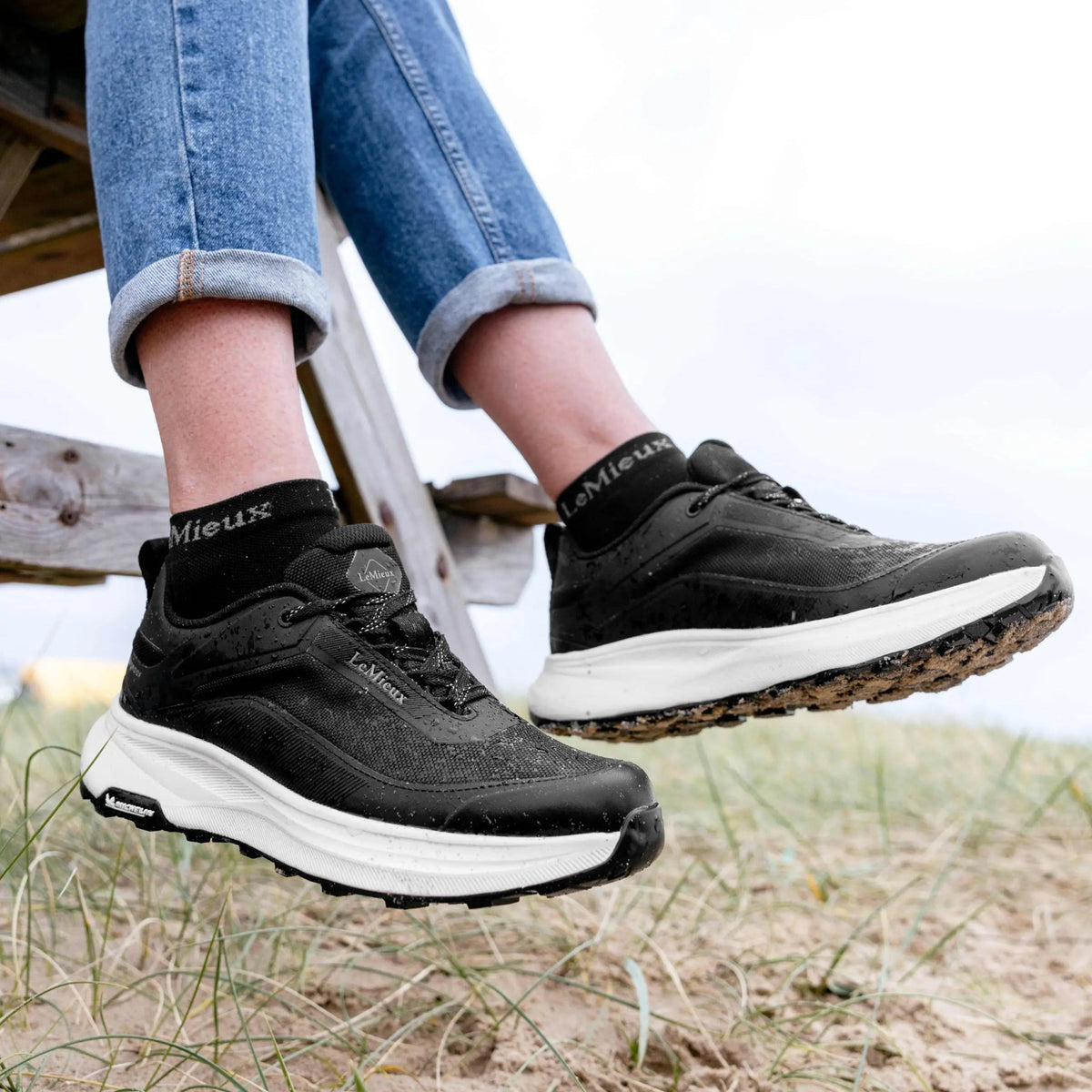 Lifestyle view of person wearing black LeMieux Kanta Waterproof Sneakers with denim jeans outdoors.