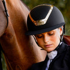 KASK Star Lady Chrome Equestrian Helmet - Black with Gold Frame;  close up shown on woman outdoors next to horse | Wide Brim English Riding Helmets | Malvern Saddlery