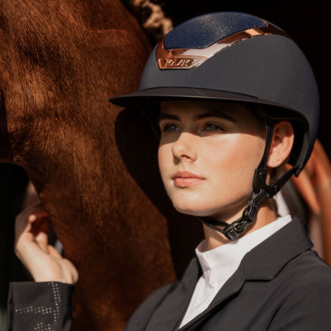 KASK Star Lady Chrome Equestrian Helmet - Navy with Rose Gold Frame;  close up shown on woman outdoors next to horse | Wide Brim English Riding Helmets | Malvern Saddlery